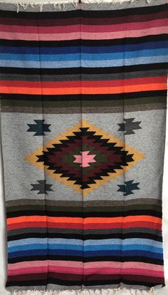 a multicolored blanket with fringes hanging on the wall