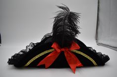 Complete your look this season with this Womens Soft Black Bicorn Pirate Hat. Perfect for Halloween, Cosplay, Theater and more! Each Buccaneer hat features a soft polyester hat with a velveteen look that has black lace trim, a gold ribbon trim, a black fake feather and accented with a red bow on both sides. Each hat is soft and does not have any wire in the brim. Lightweight and comfortable to wear, this hat is sized about 60 cm or 7 3/8th. This black pirate hat stands about 5 inches tall (not including the feather). The bicorn hat has a width of 19 inches and the shown brim is about 6 inches wide. For ages 14 and older. Spot clean only. ⭐Womens Soft Black Bicorn Pirate Hat. Features a soft polyester hat with a velveteen look that has black lace trim, a gold ribbon trim, a black fake feath Bicorn Hat, Black Pirate, Pirate Hat, Sewing Equipment, Pirate Hats, Hat Stands, Gold Ribbon, Costume Hats, Gold Ribbons