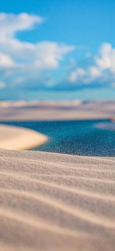 a blurry photo of sand and water under a blue sky with clouds in the background