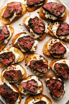 a white plate topped with mini steaks covered in cream cheese and chives on top of toasted bread