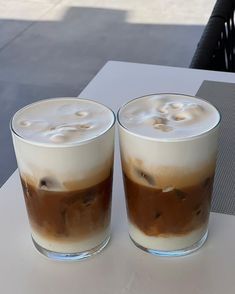 two glasses filled with liquid sitting on top of a white table next to each other