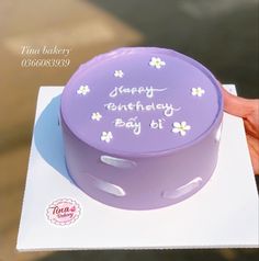 a purple birthday cake with daisies on it sitting on top of a white box