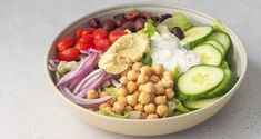 a salad with cucumbers, tomatoes, olives, lettuce and chickpeas