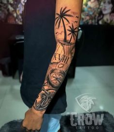 a man's arm with a compass and palm trees tattoo on the left forearm