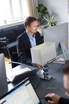 two men sitting at a desk in front of computer monitors and laptops - stock photo - images