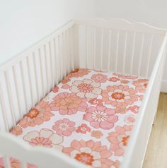 a white crib with pink and orange flowers on the bed sheet in front of it