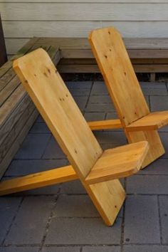 two wooden chairs sitting next to each other on top of a brick floor near a house