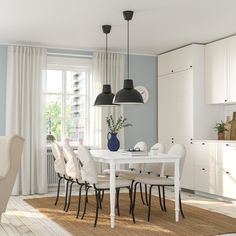 a white table and chairs in a room with light blue walls, wooden floors and large windows