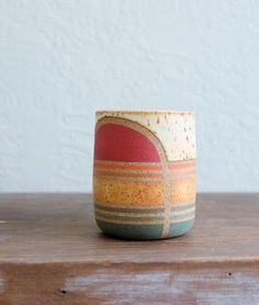 a small ceramic cup sitting on top of a wooden table next to a white wall