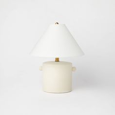 a white table lamp with a gold base and a white shade on the top, against a white background