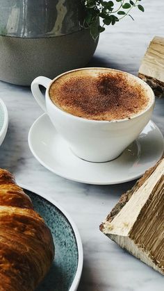 there is a cup of coffee and croissants on the table next to each other