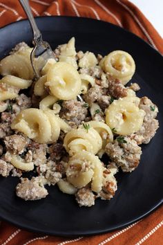 a black plate topped with pasta and meat covered in gravy next to a fork