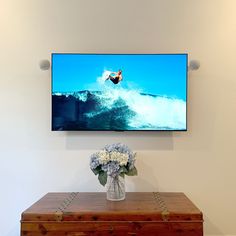 a large flat screen tv mounted on the wall above a dresser with flowers in front of it