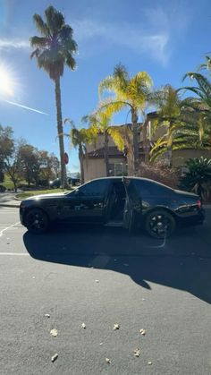 a black car parked in the middle of a parking lot with palm trees behind it