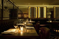 a dimly lit dining room with wine bottles on the wall and tables in front of it