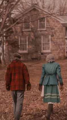 two people walking in front of a brick house on a leaf covered field next to a fire hydrant