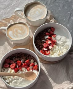 three bowls filled with cereal and strawberries next to two cups of cappuccino