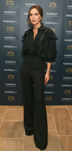 a woman standing in front of a blue wall wearing black pants and a black blouse