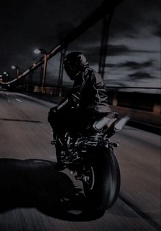 a man riding on the back of a motorcycle down a street at night with its lights on