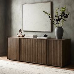 a vase with some flowers sitting on top of a wooden cabinet next to a mirror