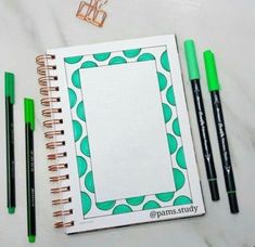 an open notebook with green markers and pencils next to it on a marble surface