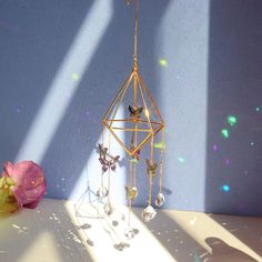 a gold and crystal wind chime hanging on a wall next to a pink flower