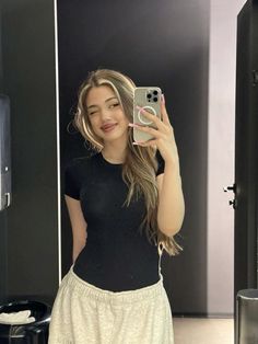 a woman taking a selfie in front of a mirror wearing a black shirt and white skirt