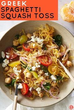 a bowl filled with spaghetti and vegetables on top of a white table next to an orange slice