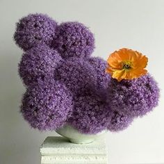 there is a purple vase with an orange flower in it on a white table top