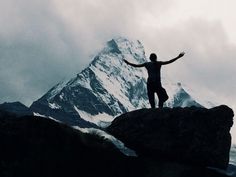 a man standing on top of a large rock with his arms wide open in front of a snow covered mountain