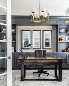 an office with gray cabinets and a wooden desk in front of two framed pictures on the wall