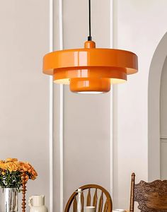 an orange pendant light hanging over a dining room table with chairs and vases on it