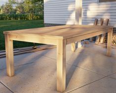 a wooden table sitting on top of a patio next to a house with grass and bushes