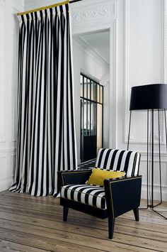 a black and white striped chair sitting in front of a window next to a lamp