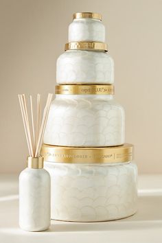 a three tiered white cake with gold trimmings and a reed diffuser