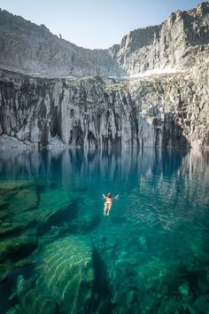 a person swimming in the water near some rocks and cliffs, with clear blue water