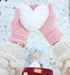 a person holding a heart shaped pillow in their hands while standing on snow covered ground