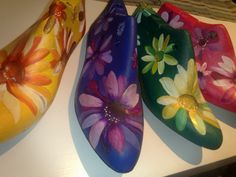 four painted shoes sitting on top of a white table next to each other and one has a flower design on it