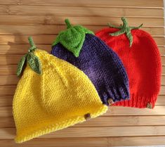 three knitted hats sitting on top of a wooden table next to each other and one has a green leaf