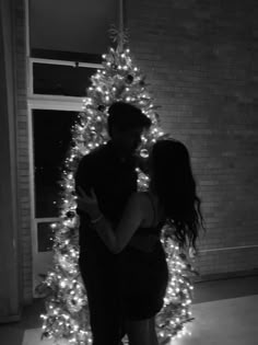 a man and woman standing in front of a christmas tree with their arms around each other