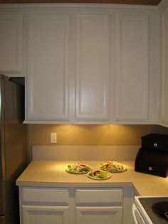 two plates of food are sitting on the counter top in this kitchen with white cabinets