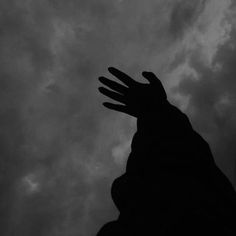 a silhouetted hand reaching up into the sky with dark clouds in the back ground