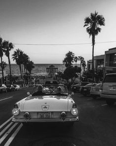 black and white photograph of an old car driving down the street with palm trees in the background