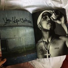 a person laying on a bed with a book open to show an image of a shirtless man drinking from a bottle