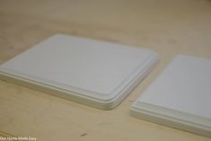 two white square coasters sitting on top of a wooden table next to each other