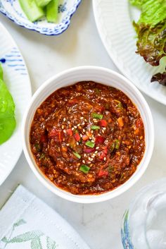 a white bowl filled with chili and lettuce on top of a table next to plates