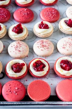 there are many red and white macaroons on the baking sheet with raspberry toppings