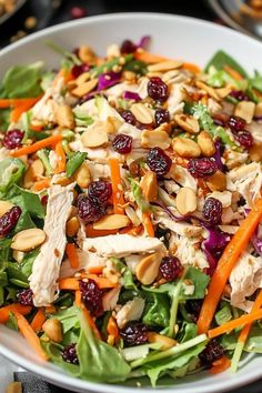 a salad with chicken, cranberries and almonds in a white bowl on a table