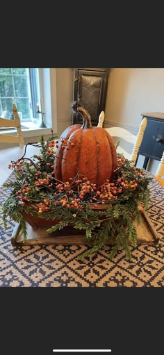 a large pumpkin sitting on top of a wooden tray filled with berries and greenery