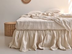 an unmade bed with white linens and a basket on the floor next to it